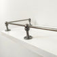 Close-up view of a Black Shadow solid brass corner post and rod assembly mounted on the edge of a white shelf.