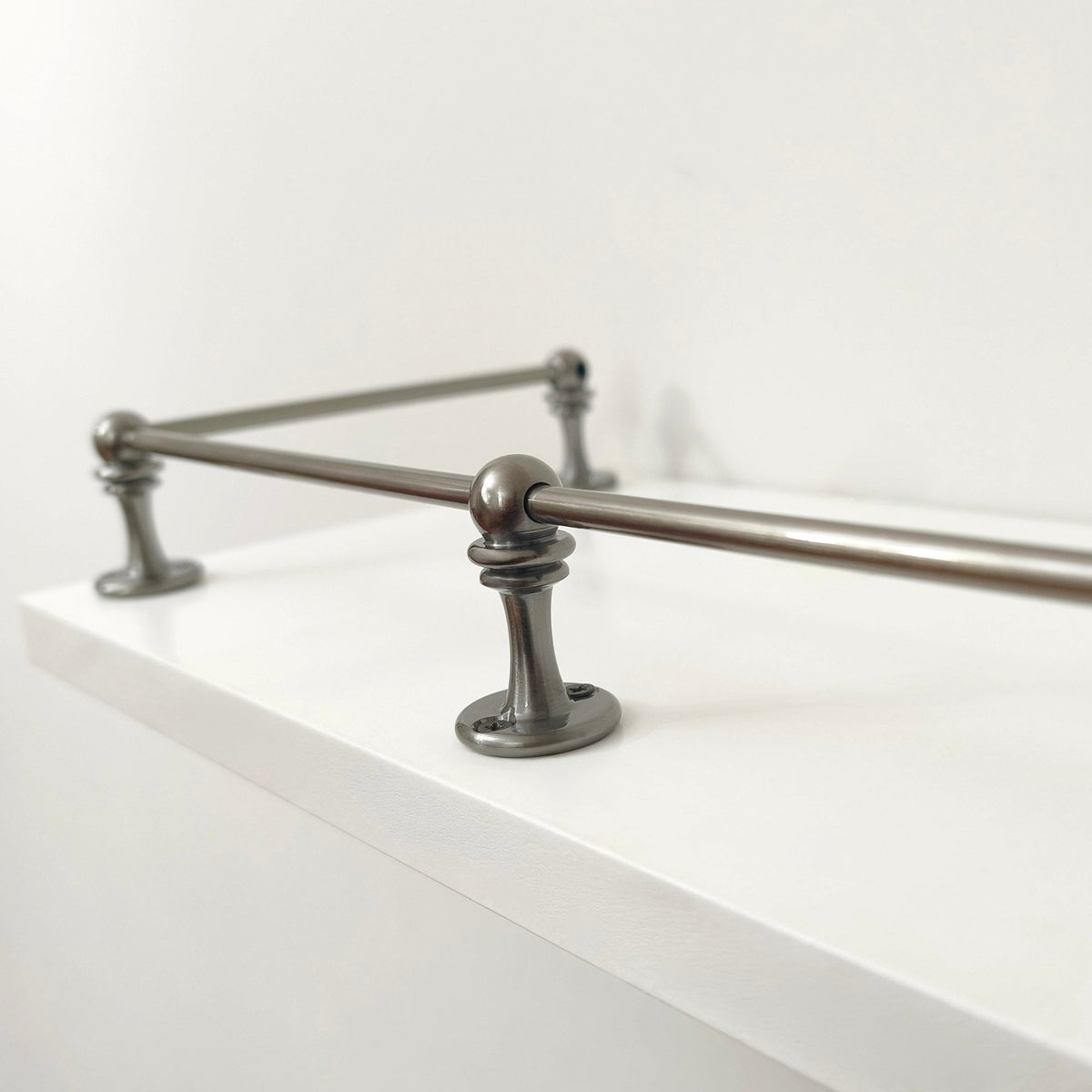Close-up view of a Black Shadow solid brass corner post and rod assembly mounted on the edge of a white shelf.
