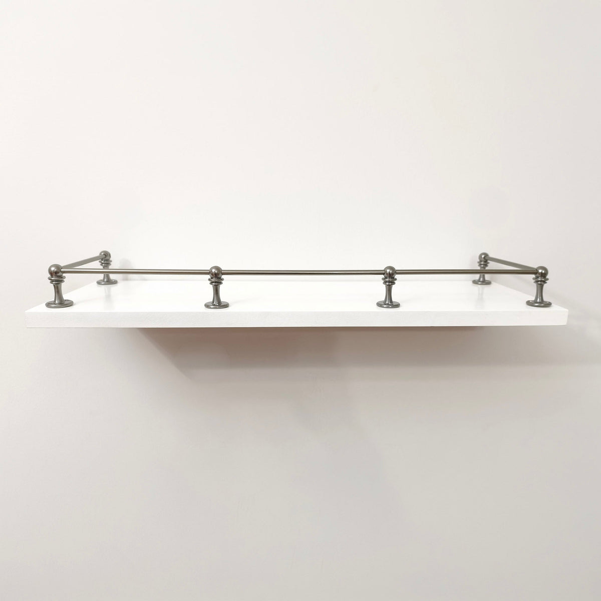 Straight front eye-level view of Black Shadow solid brass gallery railing system mounted on a floating white wall shelf.