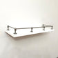 Full front angle view of a Black Shadow solid brass gallery rail system installed around three sides of a white floating shelf.