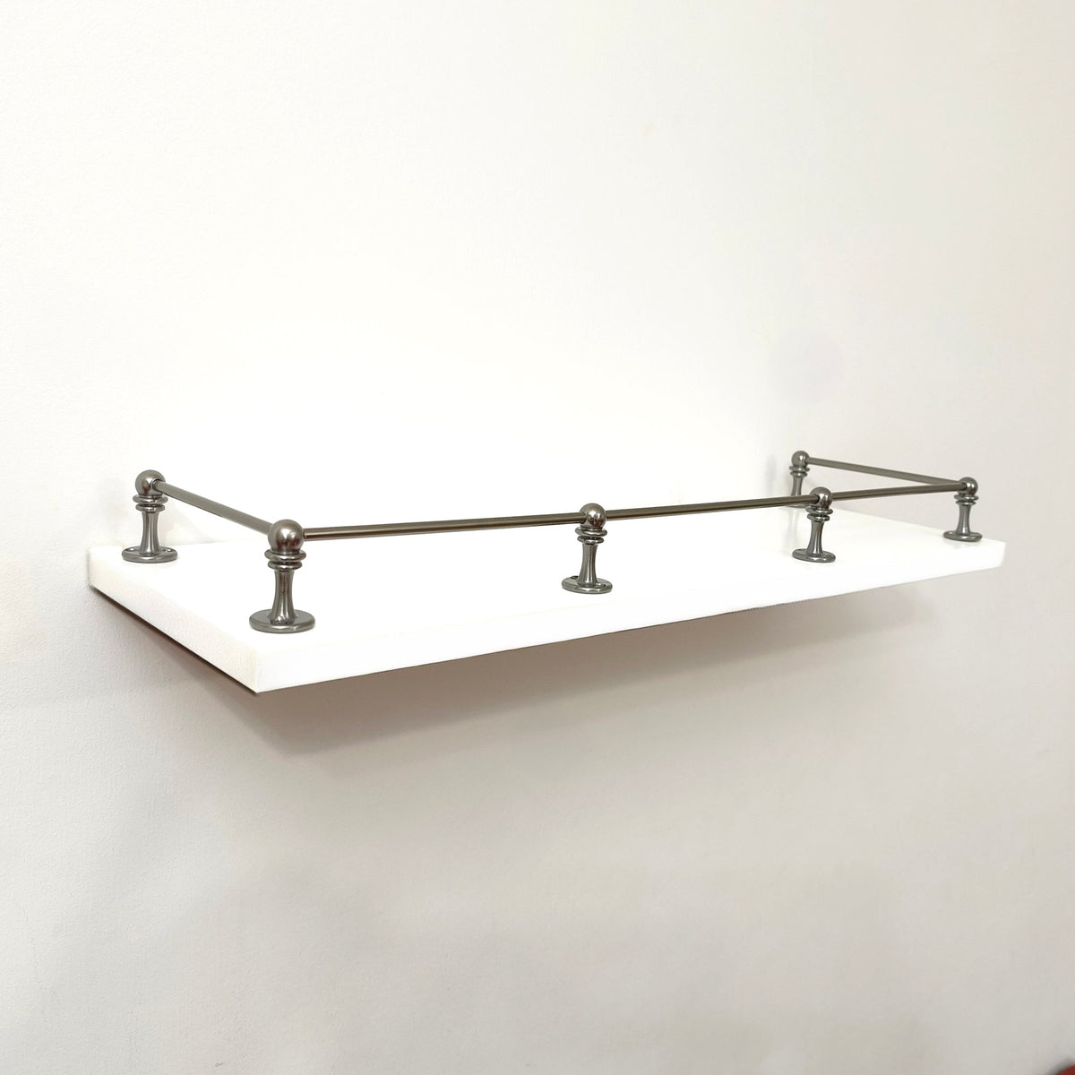 Full front angle view of a Black Shadow solid brass gallery rail system installed around three sides of a white floating shelf.