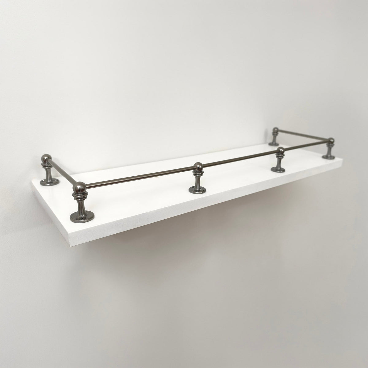 A clean, three-quarter perspective view of the fully installed Black Shadow solid brass gallery rail system on a white floating shelf, showing its sleek, dark finish without any text labels.