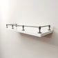 Black Shadow solid brass gallery rail system with corner and middle posts mounted on a floating white wall shelf.