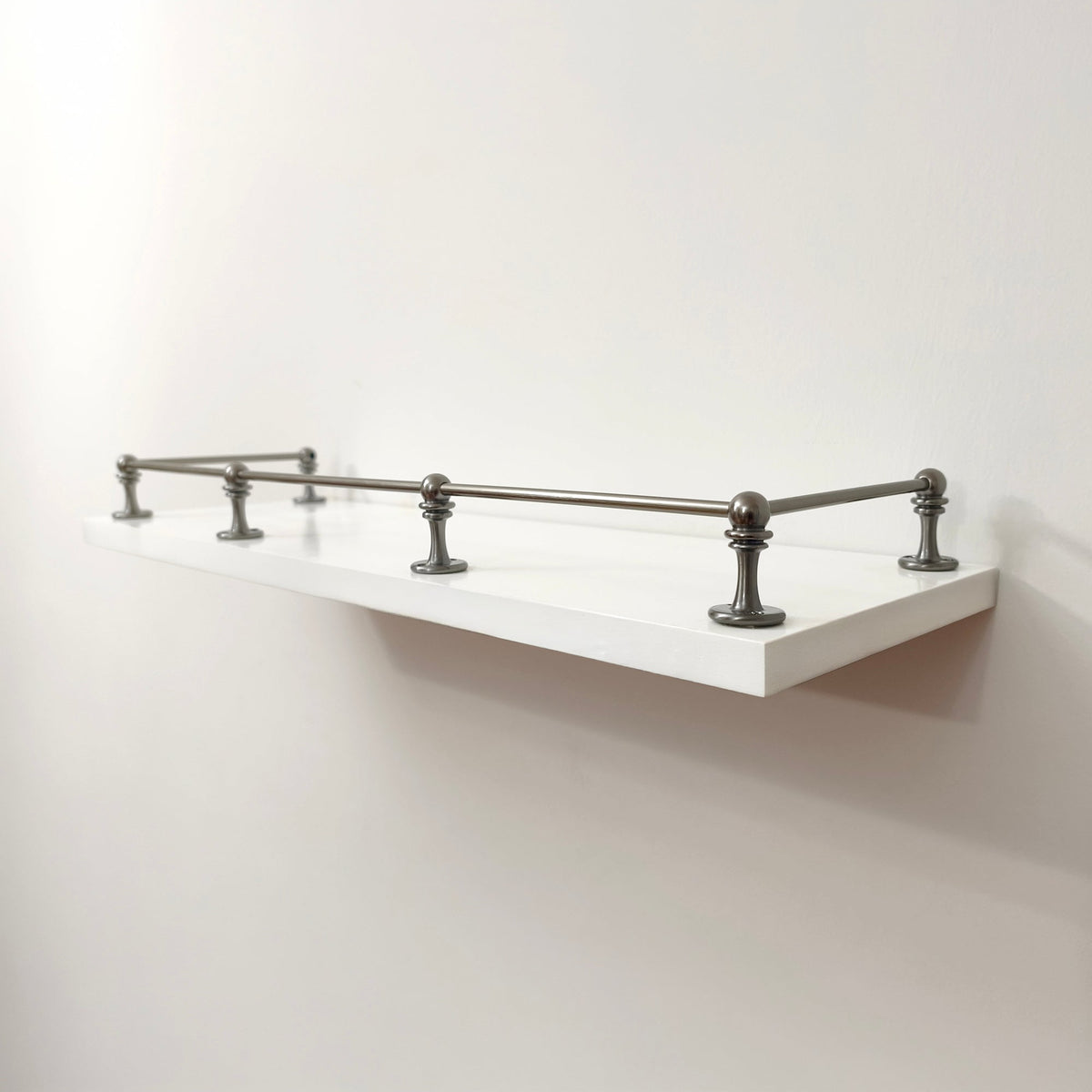 Black Shadow solid brass gallery rail system with corner and middle posts mounted on a floating white wall shelf.
