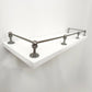 Perspective side view of Black Shadow solid brass gallery rail mounted on a white floating shelf focusing on the front corner post.