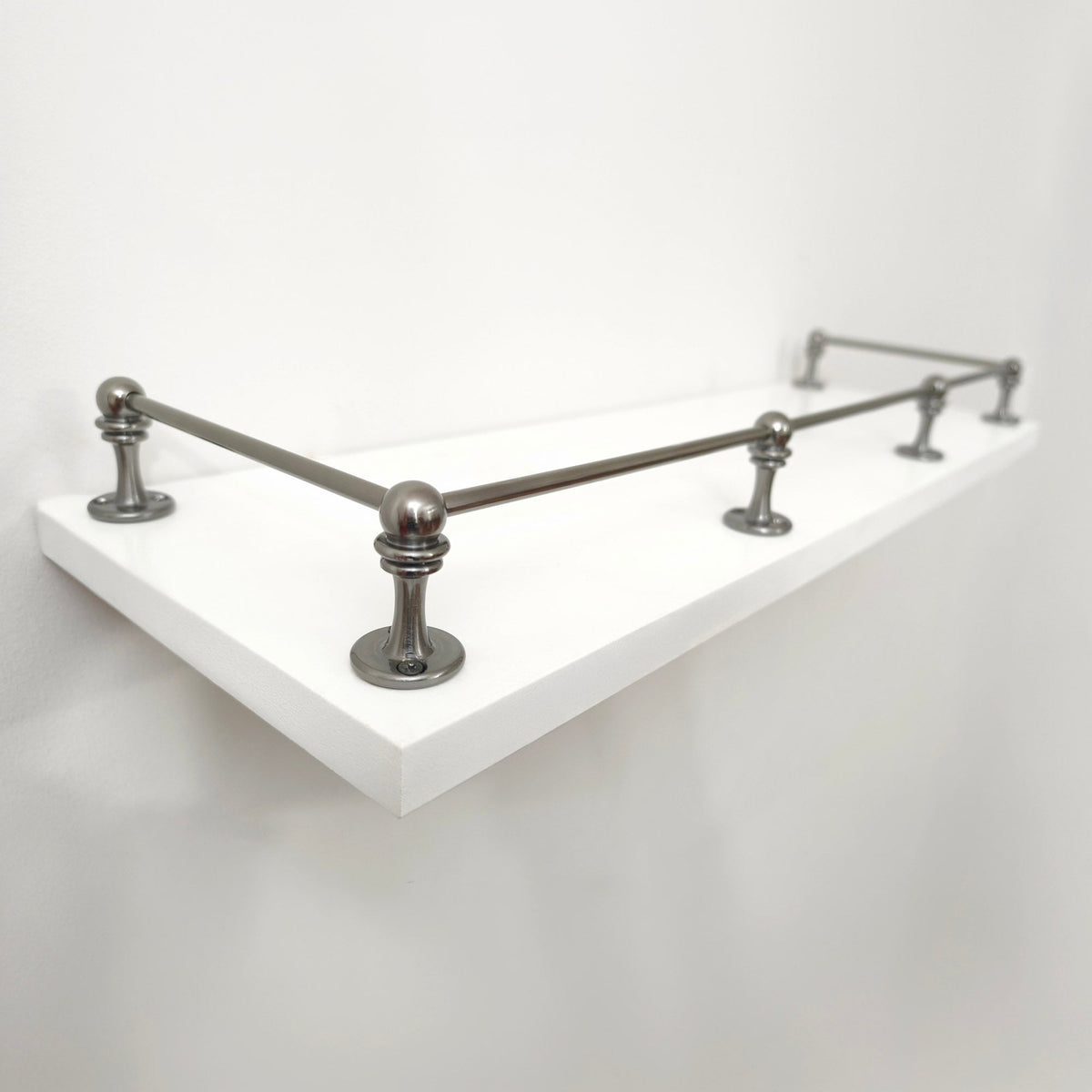 Perspective side view of Black Shadow solid brass gallery rail mounted on a white floating shelf focusing on the front corner post.