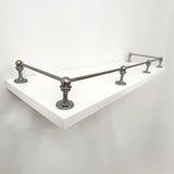 Perspective side view of Black Shadow solid brass gallery rail mounted on a white floating shelf focusing on the front corner post.
