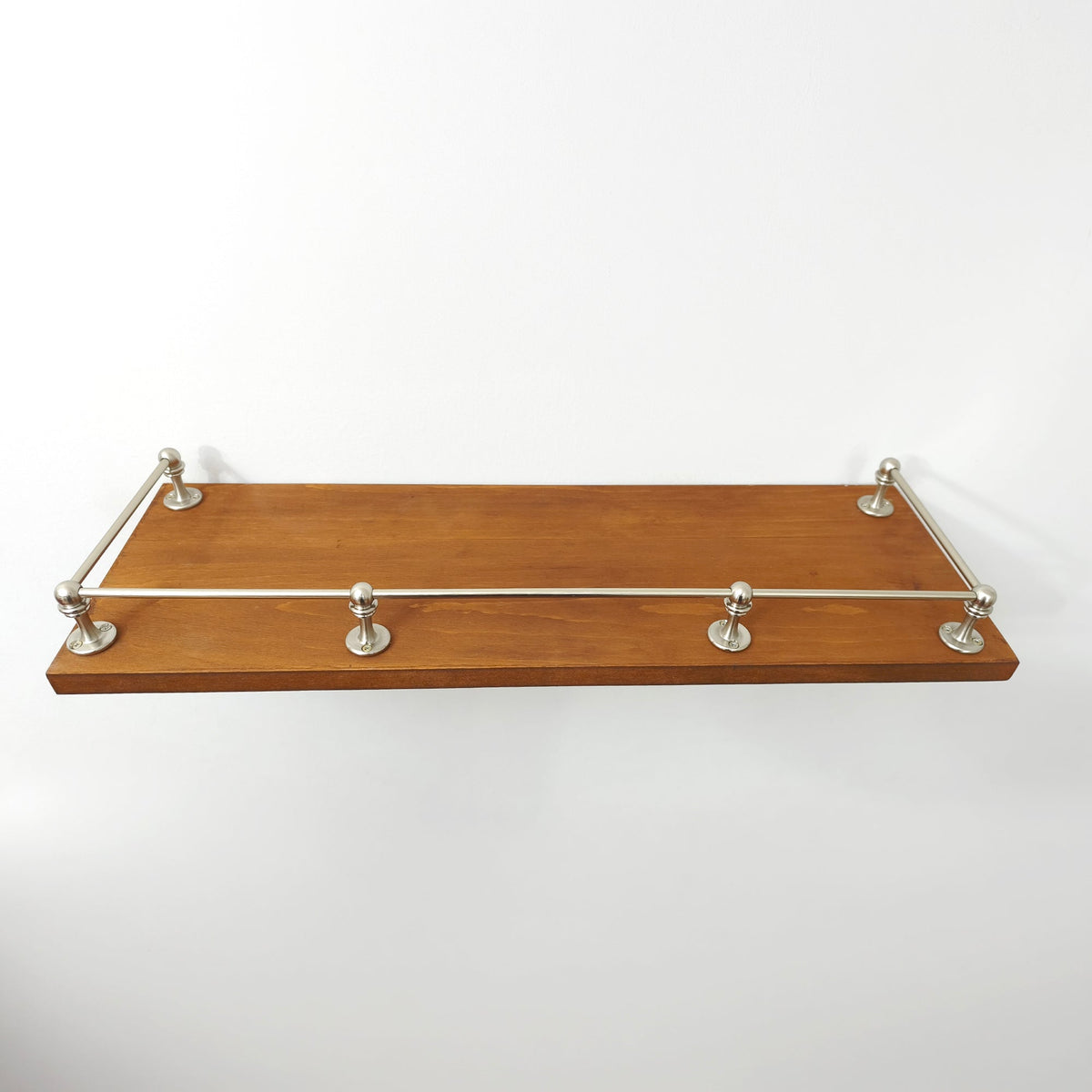 Front view of brushed nickel brass gallery rail installed along the front and side edges of a wooden shelf.