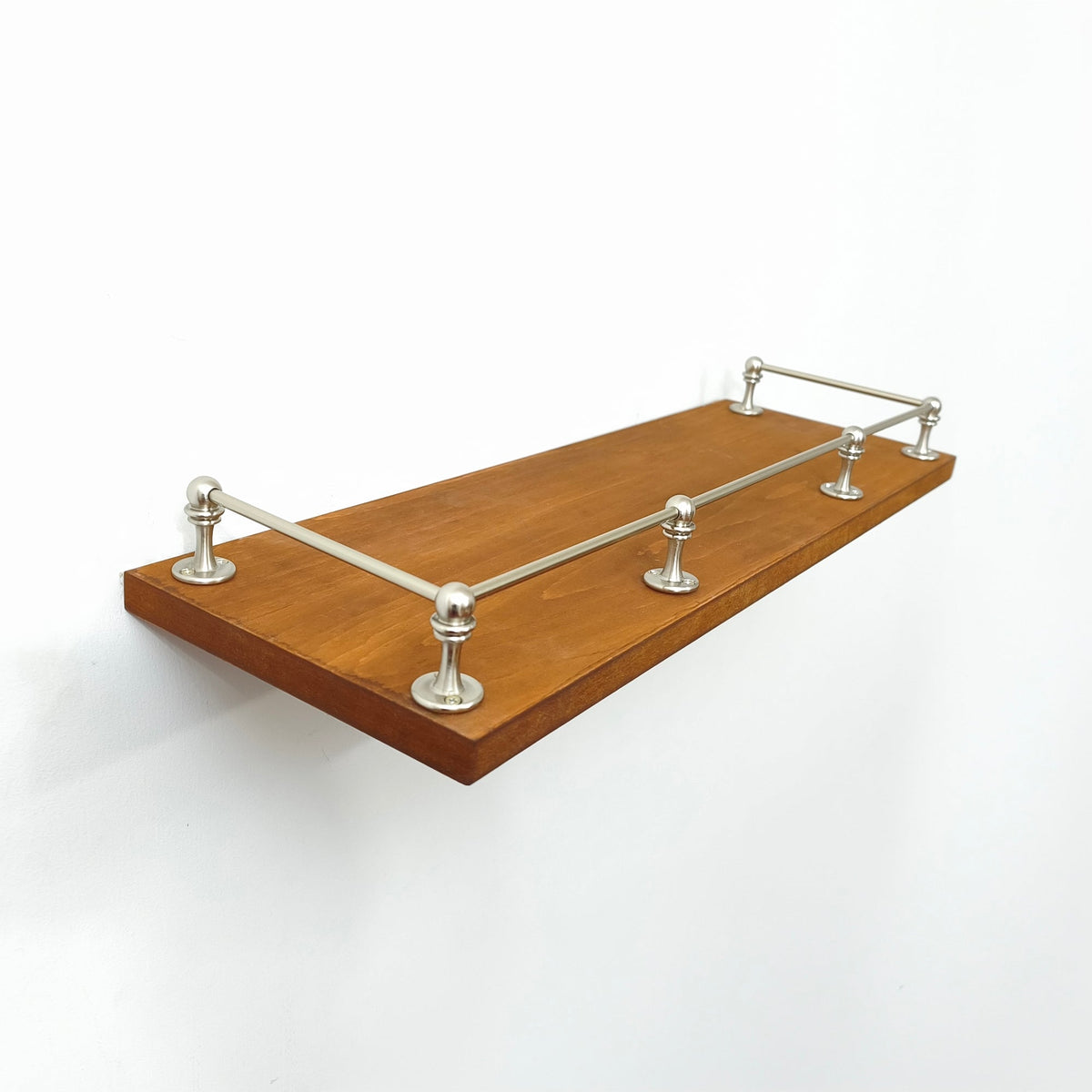 Brushed nickel brass gallery rail system installed on front and sides of a floating wooden shelf.