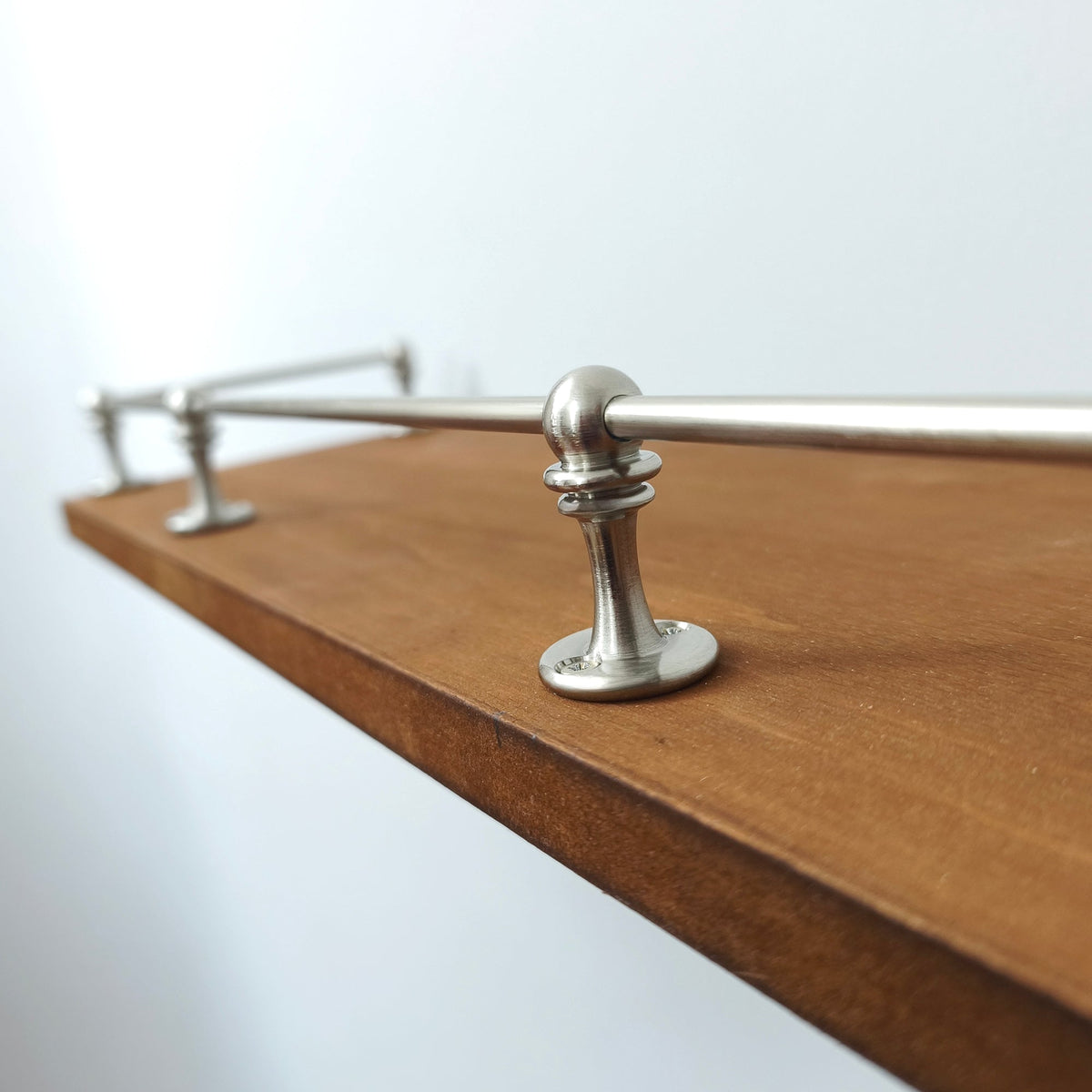 Close-up detail of a brushed nickel solid brass gallery rail post and rod mounted on a wooden shelf.