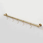 Front-angle view of a compact solid unlacquered brass kitchen hanging rod with five S-hooks mounted on a white wall.