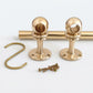 Unlacquered brass kitchen rail hardware kit featuring a solid brass rod, two spherical mounting posts, a matching S-hook, and installation screws, all displayed on a white surface.