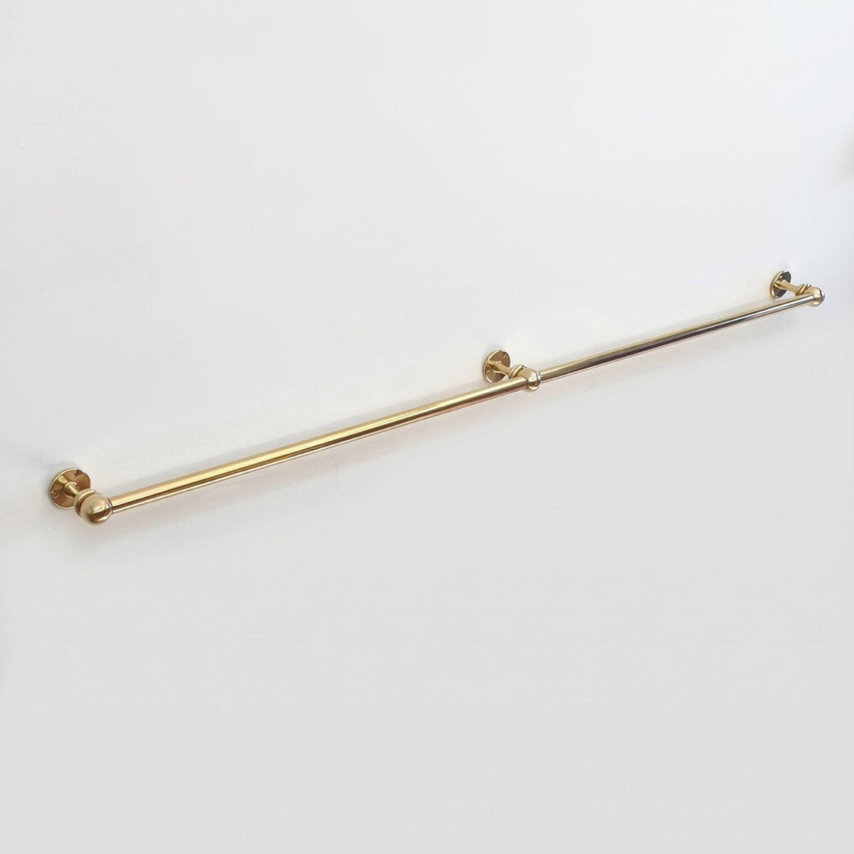Side angle view of an extra long wall-mounted unlacquered solid brass kitchen rail with center support post on a clean white background.