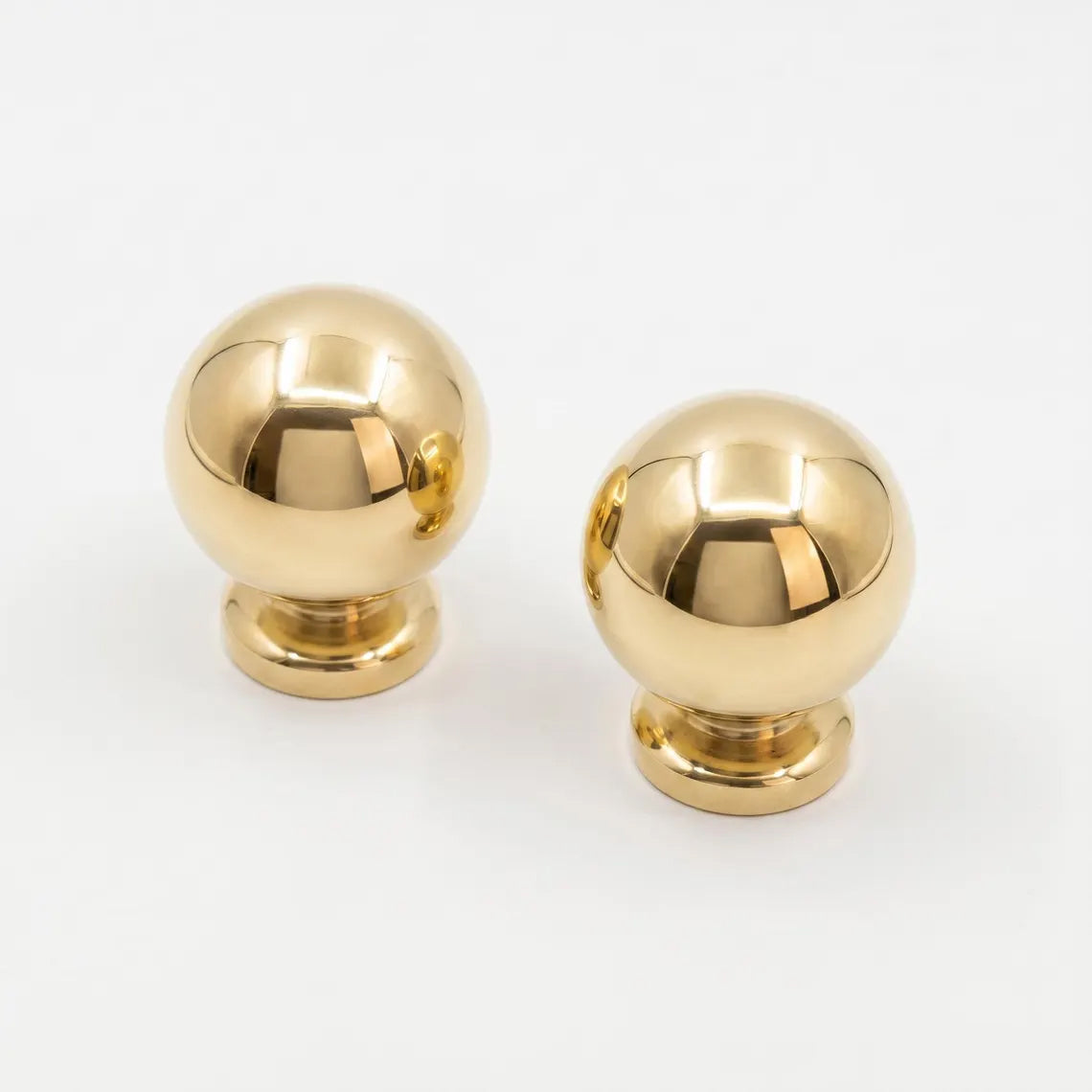 Pair of unlacquered solid brass spherical ball cabinet knobs with polished finish on clean white background.