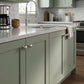 Brushed satin nickel solid brass ball cabinet knobs installed on sage green shaker kitchen island cabinets with marble countertops.