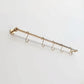 Perspective view of a short solid unlacquered brass kitchen hanging rail mounted on a plain white surface with five matching S-hooks.