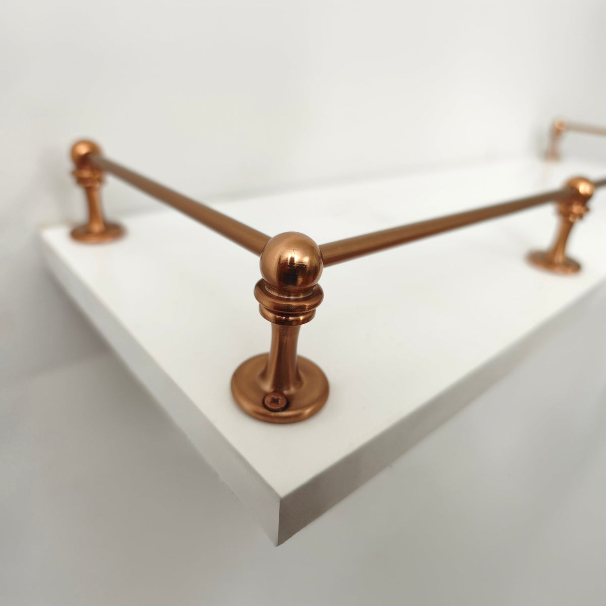 Brass Gallery Rail solid brass gallery rail in a warm copper finish, close-up perspective view of the 90-degree corner post mounted on a white wall shelf.