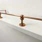 Brass Gallery Rail solid brass gallery rail with warm copper finish, close-up view of the through post mounted on a white wooden shelf. – view 5