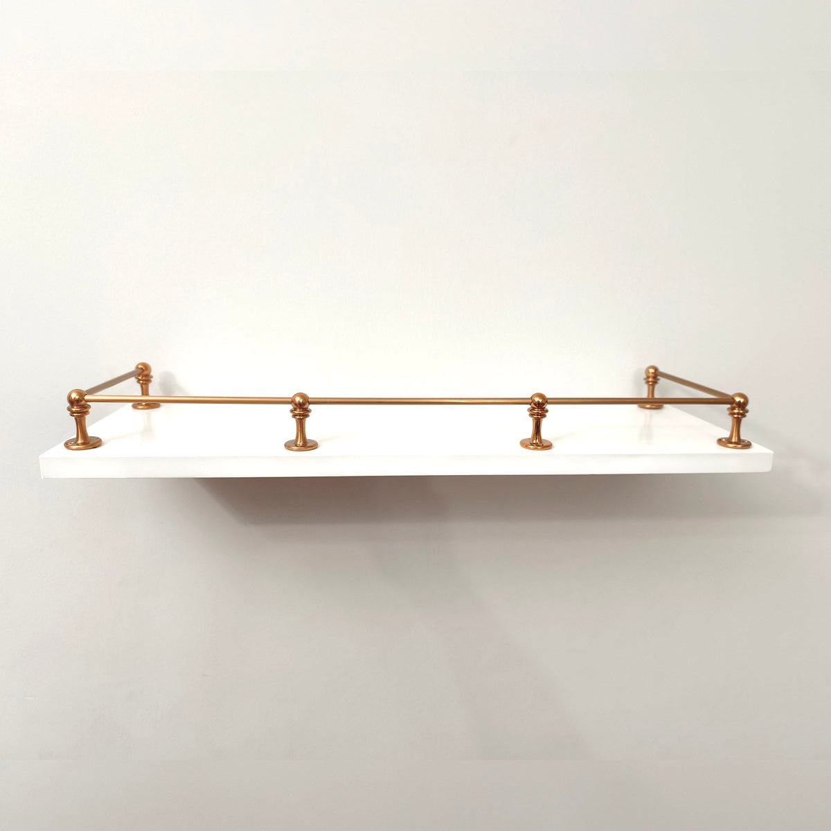 Brass Gallery Rail solid brass gallery rail set with warm copper finish, front view mounted on a floating white wall shelf. – view 4