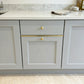 Solid brass drawer topper flat profile installed on light grey shaker cabinets with round brass knobs and marble countertop.