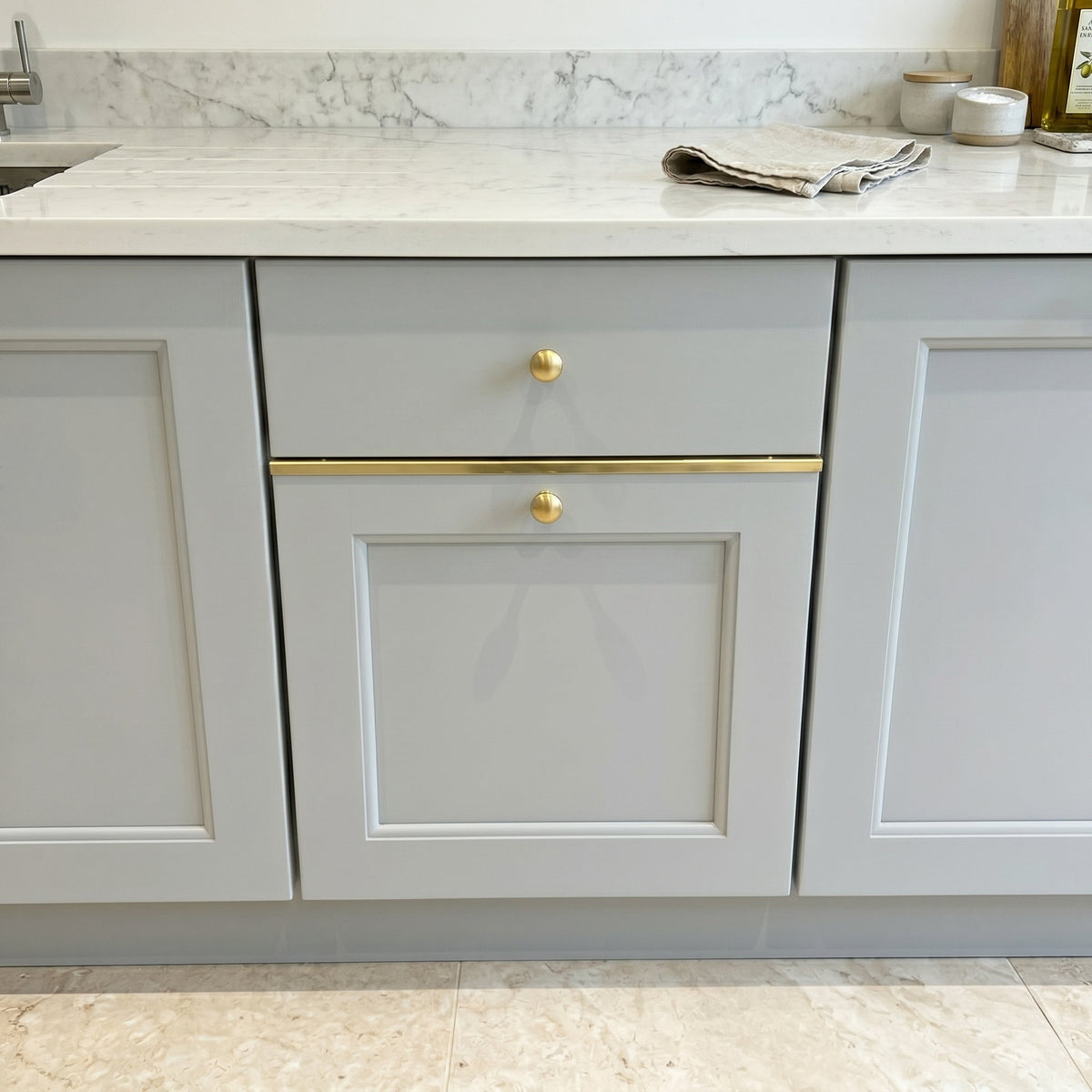 Solid brass drawer topper flat profile installed on light grey shaker cabinets with round brass knobs and marble countertop.