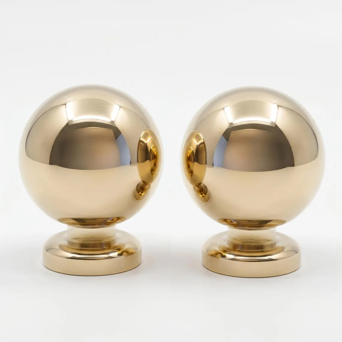 Close-up studio shot of a pair of polished unlacquered solid brass ball drawer knobs on a seamless white background.