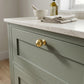 Unlacquered satin brass solid ball drawer knob installed on a sage green shaker cabinet vanity with a white marble countertop.