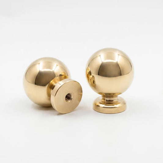 Pair of unlacquered solid brass ball drawer knobs showing front view and threaded bottom base on white background.