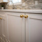 Unlacquered polished solid brass spherical ball knobs installed on classic white shaker kitchen cabinets with quartz countertop.