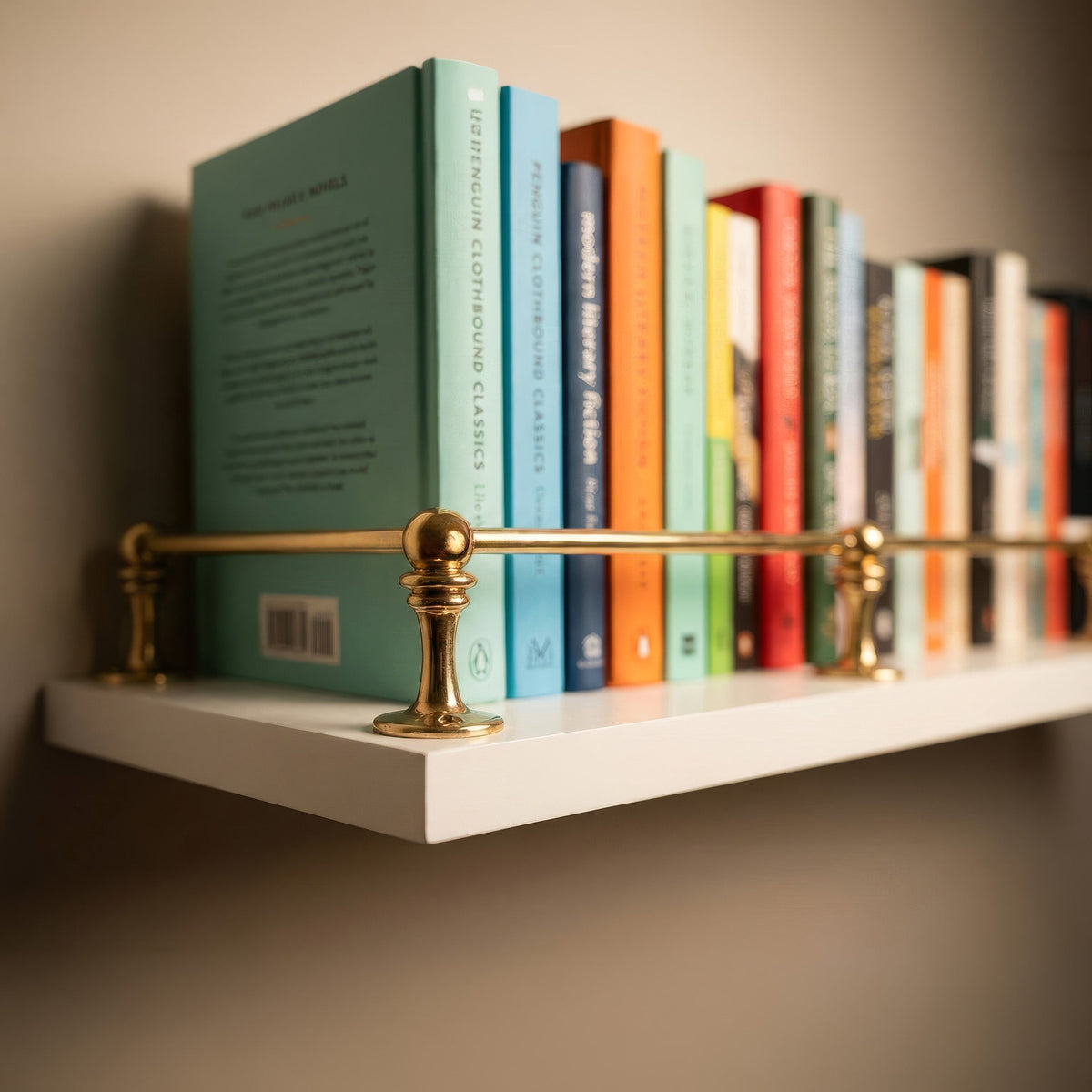 Close-up of an unlacquered solid brass gallery rail mounted on a white wall floating shelf holding colorful books.