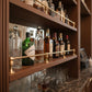 Solid unlacquered brass gallery rail installed on multi-tier wooden commercial bar shelves holding liquor bottles and glassware.