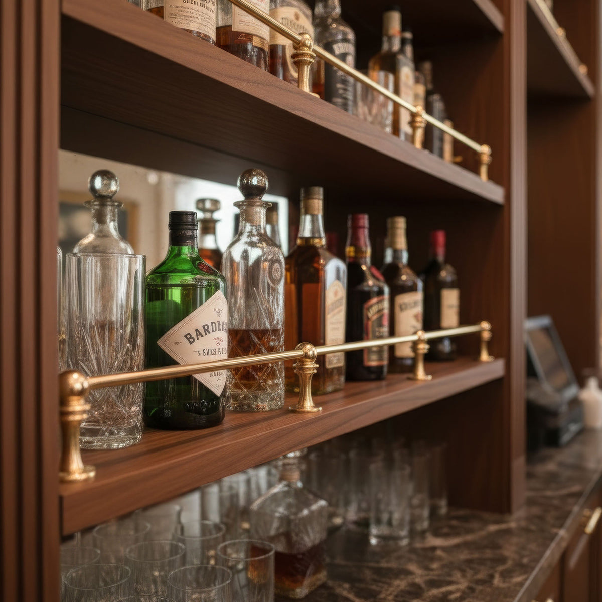 Solid unlacquered brass gallery rail installed on multi-tier wooden commercial bar shelves holding liquor bottles and glassware.
