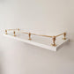 Polished unlacquered solid brass gallery rail system mounted on a sleek white floating wall shelf.