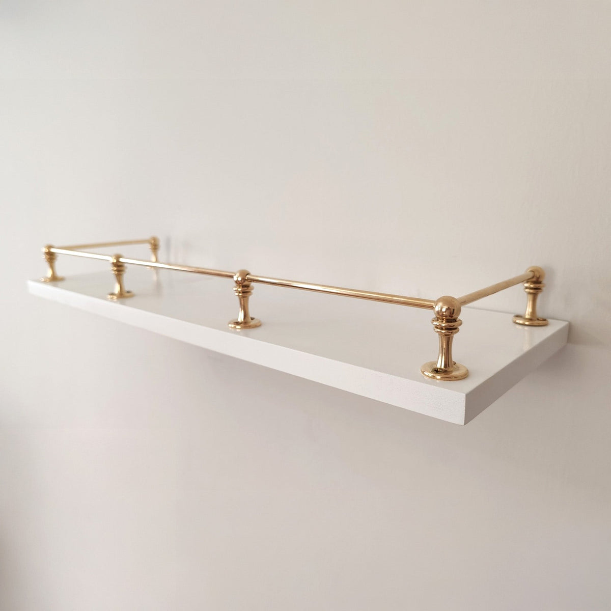 Polished unlacquered solid brass gallery rail system mounted on a sleek white floating wall shelf.