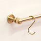 Detailed close-up of a solid unlacquered brass kitchen rail end bracket with a spherical ball finial and hanging brass S-hook on a white wall.